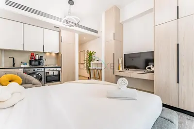 a white bedroom with a large bed and a kitchen at Studio with Community Views, Easy Access to Bus Stop, Parks, and Circle Mall, Empire Residence, JVC by Deluxe Holiday Homes in Dubai