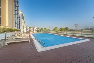 a swimming pool with benches next to a building at Stylish 1BR with Pool Gym and Parking in Riviera 12 in Dubai
