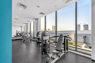 a gym with rows of tread machines and windows at Stylish 1BR with Pool Gym and Parking in Riviera 12 in Dubai