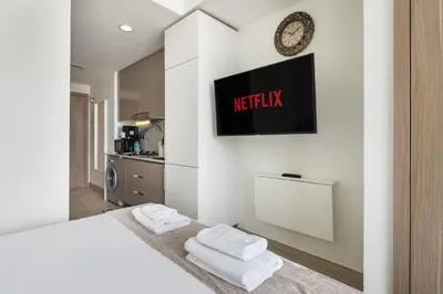a white bedroom with a bed and a tv on the wall at Stylish Studio Apartment in Azizi Riviera One in Dubai