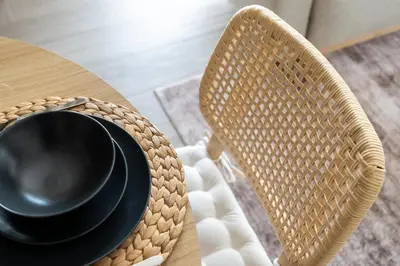 a table with a black plate and a wicker chair at GuestReady - Coastal Style l 2Bed l Lagoon Escape in Dubai