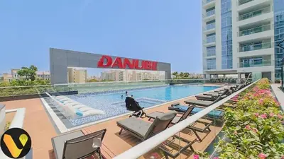 a swimming pool with lounge chairs and a building at Vogue Al Furjan Pearlz by Danube near Ibn Battuta Mall, One Bedroom Apartment with Balcony and Pool View, Access to all Amenities, Walkable to Al Furjan Metro Station in Dubai