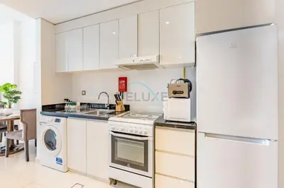 a kitchen with white cabinets and a refrigerator at Studio Overlooking the Pool, Close to Parks, Grocery Stores, and Circle Mall, Damac Ghalia, JVC by Deluxe Holiday Homes in Dubai