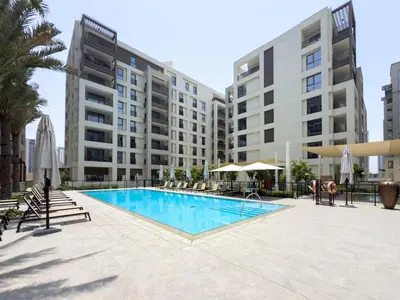 a swimming pool with chairs and umbrellas and buildings at GuestReady - 1Bed l Lagoon Escape l Creek Beach in Dubai