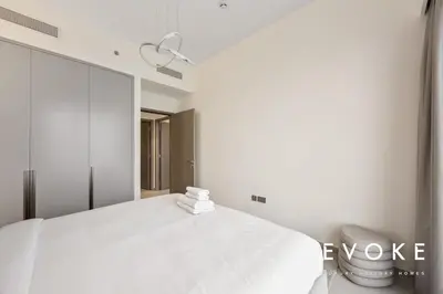 a white bedroom with a bed and a mirror at Grande 2BR Balcony Burj & Fountain Views by Evoke in Dubai