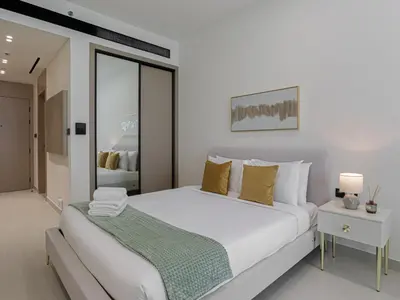 a white bedroom with a large white bed with yellow pillows at Welhome - Modern Gold Accents Studio in JVC with Balcony in Dubai