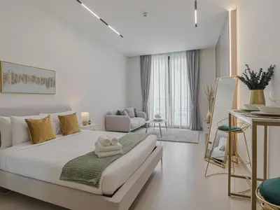 a white bedroom with a bed and a living room at Welhome - Modern Gold Accents Studio in JVC with Balcony in Dubai