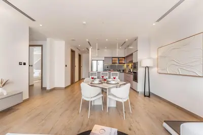 a white kitchen and dining room with a table and chairs at 2BDR with Pool, Sauna and PS5 - Near Circle Mall in Dubai