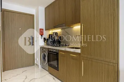 a kitchen with wooden cabinets and a washer and dryer at Bloomfields Supreme Stu In Azizi Riviera in Dubai