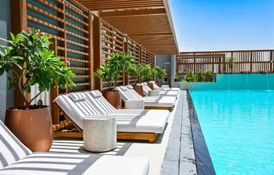 a row of chaise lounge chairs next to a swimming pool at Modern 1BR w Balcony & Great Amenities JVC in Dubai