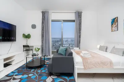 a white bedroom with a large bed and a tv at White Sage Modern Studio in JVC with Balcony and City Views in Dubai