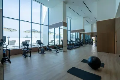a gym with a lot of exercise equipment and windows at Modern 1BR Apt in Binghatti Gardenia with Pool & Gym! in Dubai
