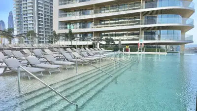 a pool of water with chairs in front of a building at Elegant 2BR, Grand Bleu, Coastal Elegance in Dubai