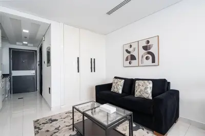 a living room with a black couch and a glass table at Sleek and Spacious Sports City Studio in Dubai