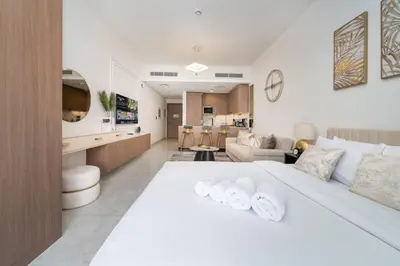 a bedroom with a white bed and a living room at Stylish Studio in JVC Bright, Cozy and Convenient in Dubai