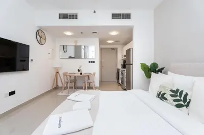 a white bedroom with a white bed and a table at Gala Guests - Serene Lakeside Residences Production City in Dubai