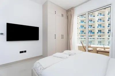 a white bedroom with a bed and a tv at Gala Guests - Serene Lakeside Residences Production City in Dubai