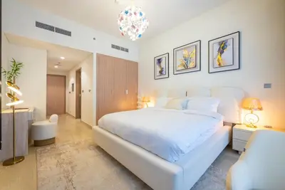 a white bedroom with a large bed and a chair at Cozy Studio with a huge terrace in Dubai