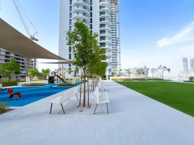 a park with white benches and trees in front of a building at Beachfront 1B at Palm Jumeirah with Balcony & Views in Dubai