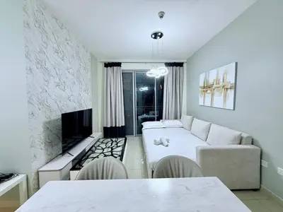 a white living room with a couch and a tv at Urban Retreat 1BR with Pool & Burj Glimpse in Dubai