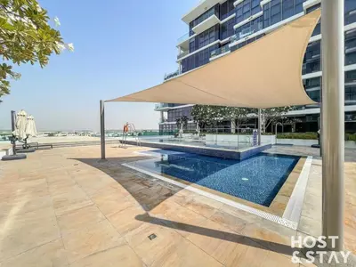a pool in front of a building with a large umbrella at Modern Studio in Loreto 1A, Damac Hills in Dubai