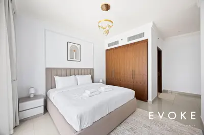 a bedroom with a large white bed with a wooden door at Luxury 2BR by Evoke Burj & fountain View w Sofa bed & Balcony in Dubai