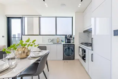 a white kitchen with a dining table and chairs at Modern 2BR with Private Pool, Near Circle Mall And Quick Access from Al Khail Road, Binghatti Tulip, JVC by Deluxe Holiday Homes in Dubai