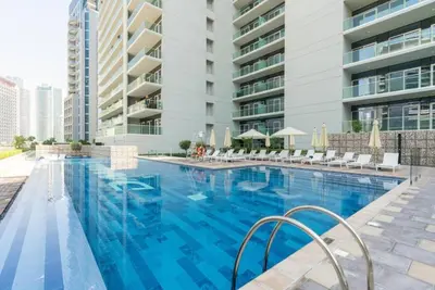 a large swimming pool with chairs and a building at Cosy 2BR Business Bay with Canal view and Swimming pool in Dubai