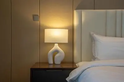 a white lamp on a table next to a bed at Samaya Holiday Homes - Modern Luxe Apartments - Nobles Tower in Dubai