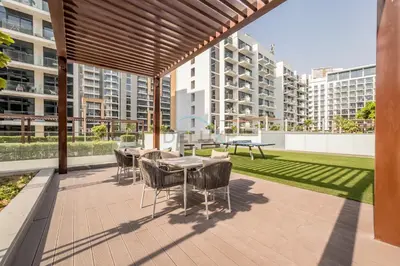 a patio with tables and chairs and a lawn with buildings at Close to Meydan Racecourse and Ras Al Khor Wildlife Sanctuary, And a Quick Drive to Downtown Dubai and the Iconic Burj Khalifa - Azizi Riviera 44, Meydan by Deluxe Holiday Homes in Dubai