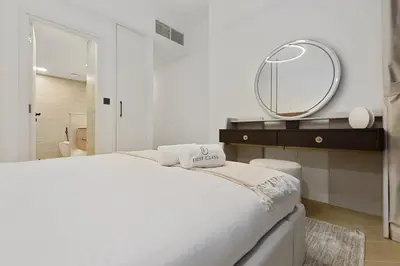 a white bedroom with a bed and a mirror at FIRST CLASS 2BR Burj Views & Classy Comfort in Dubai