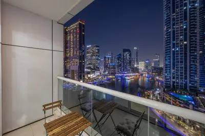 a balcony with two chairs and a city skyline at night at Exceptional 2BR with Marina Waterfront View in Dubai