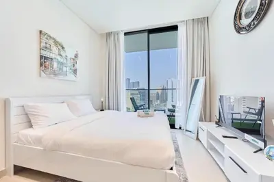 a white bedroom with a bed and a large window at FAM Living Stylish Studio Apartment in Binghatti Azure JVC in Dubai
