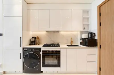 a kitchen with white cabinets and a washer and dryer at FAM Living Stylish Studio Apartment in Binghatti Azure JVC in Dubai