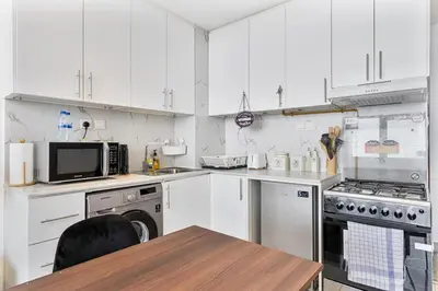 a kitchen with white cabinets and a table and a microwave at Modern Studio with City Views Near Miracle Garden in Dubai