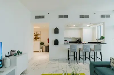 a kitchen and living room with white walls and stools at RH Luxe Vibes 2BR Al Habtoor City, Mesmerizing Canal View in Dubai