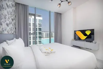 a white bedroom with a bed and a tv at Vogue Al Maktoum City, District One Residence, within a short drive from Downtown Burj Khalifa and Dubai Mall, Three Bedroom Apartment plus Kids Room with Large Balcony in Dubai