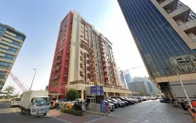 a tall red building with cars parked in a parking lot at Eco Space Partition Room in Green view 3 in Dubai