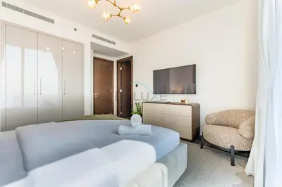 a bedroom with a bed and a tv and a chair at High-Floor 2BR with Skyline Views, Steps from a Park, Minutes Drive to Meydan Golf Club and Ras Al Khor Wildlife Sanctuary, Sobha Hartland The Crest Tower C, Sobha Hartland by Deluxe Holiday Homes in Dubai