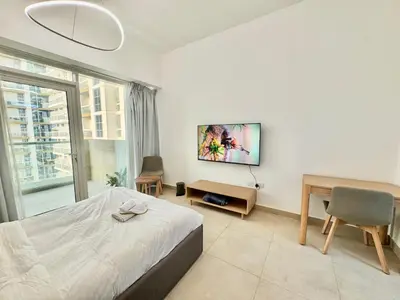 a bedroom with a bed and a desk and a window at Homes2Retreat - Cozy Studio with Pool and Sauna in Al Furjan in Dubai