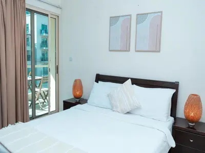 a bedroom with a white bed and a balcony at Bright & Spacious 2BR Apartment | The Greens Community in Dubai