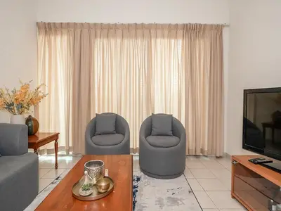 a living room with two chairs and a television at Bright & Spacious 2BR Apartment | The Greens Community in Dubai