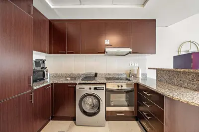 a kitchen with wooden cabinets and a washer and dryer at Silkhaus Comfy Studio in Sky Gardens with DIFC Views in Dubai
