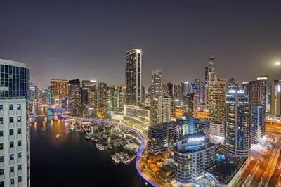 a city skyline at night with a river and buildings at Stylish 1BR Apartment with Marina View, Balcony, Pool & Gym Access in Dubai