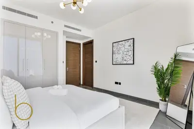 a white bedroom with a large bed and a potted plant at Bookable 2 Bed Crest Sobha Hartland with Burj view in Dubai