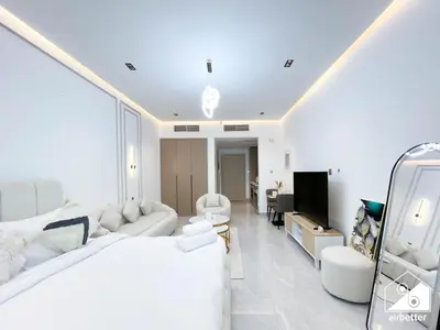 a white bedroom with a large bed and a living room at Elegant Studio with Balcony & Full Amenities in Dubai
