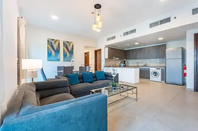 a living room with a blue couch and a kitchen at Balcony Overlooking the Community, Quick Metro Access,Short 15-Minute Drive to Ibn Battuta Mall, Viktoria Residency, Al Furjan by Deluxe Holiday Homes in Dubai