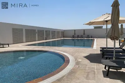 a swimming pool with an umbrella and some chairs at Mira Holiday Homes - Luxury, Stylish & Cozy Studio in Downtown Jebel Ali in Dubai