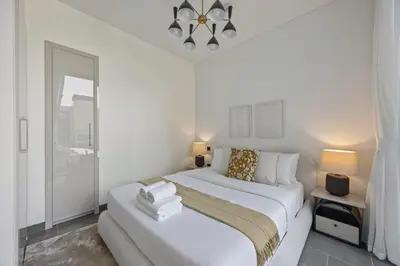 a white bedroom with a large bed and a chandelier at Modern Apartment with Balcony and Pool Access in Dubai