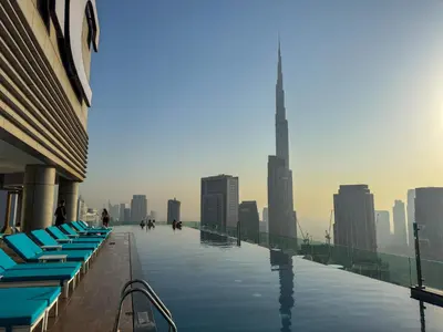 a swimming pool with blue lounge chairs and a city skyline at Paramount Midtown, Luxury 1BR with Infinity Pool with Burj View in Dubai
